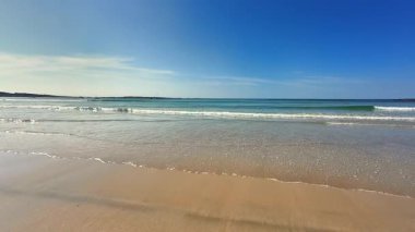 Güzel ve sakin bir sahil sahnesi. Dalgalar sahile vuruyor. Açık mavi gökyüzünün altında.