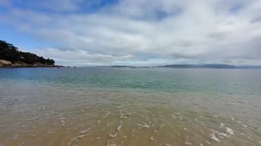Güzel, sakin bir sahil sahnesi. Hafif dalgalar, geniş kumlu kıyılar ve yukarıda resim gibi bir gökyüzü.