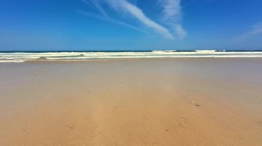 Huzurlu ve sakin bir sahil sahnesi yumuşak altın kumlar ve parlak mavi gökyüzünün altında yumuşak okyanus dalgaları.