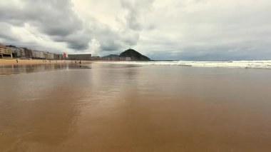 Yumuşak dalgaların, kumlu kıyıların ve dramatik, tüylü bulutların olduğu güzel, sakin bir sahil sahnesi.