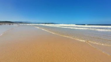 Güzel ve sakin bir sahil, yumuşak kumlu kıyılar, yumuşak okyanus dalgaları ve berrak mavi bir gökyüzü.