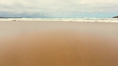 Huzurlu ve sakin bir sahil sahnesi yumuşak, sıcak altın kum üzerinde zarif dalgaların yuvarlandığı.