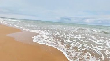 Sakin ve sakin bir sahil sahnesi, bulutlu bir günde kumlu sahilde usulca dalgalar sergiliyor.
