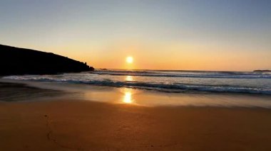 Huzurlu plajda parlayan şaşırtıcı derecede güzel bir gün batımı, yumuşak, huzurlu dalgaları ve altın kumları gözler önüne seriyor.