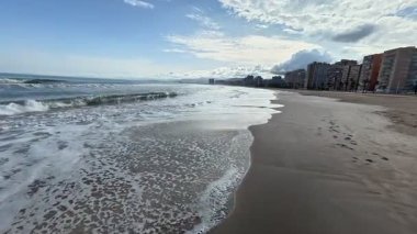 Huzurlu ve huzurlu bir sahil manzarası. Yumuşak dalgalar, altın kum ve yukarıda sakin bir gökyüzü.