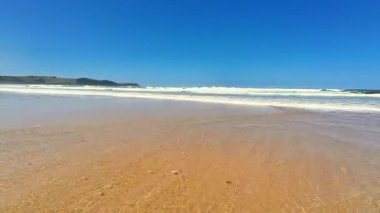 Huzurlu ve sakin bir sahil sahnesi yukardaki canlı mavi gökyüzü ile birlikte yumuşak, nazik dalgaları yakalıyor.