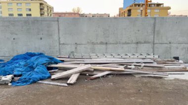 Mavi branda örtüsüyle kısmen kaplanmış ahşap döküntüleri gösteren bir inşaat alanı.