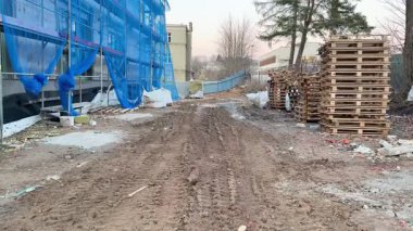 Bir inşaat alanındaki çakıllı patikada paletler ve mavi koruyucu ağ belirgin bir görünüm sergiler