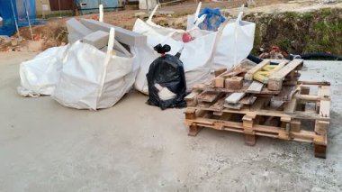 Çok sayıda atık torbası ve ahşap paletler sergilenen bir inşaat alanının geniş bir görüntüsü