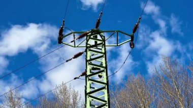 Pofuduk beyaz bulutlu açık mavi gökyüzüne karşı etkileyici bir elektrik iletim kulesi.