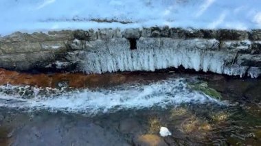 Buzlu kaya oluşumları ve akan sularla büyüleyici bir derenin sergilendiği güzel, resimli bir kış manzarası.