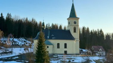 Ağaçlarla kaplı karlı bir kış manzarasında yuva yapmış, mevsimin dinginliğini yakalayan pitoresk bir kilise.