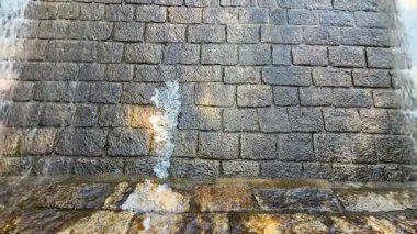 Kalıplaşmış taş bir duvar, engebeli yüzeyine doğru akan suyun akışını gösterir ve sanatsal yapısını ön plana çıkarır.