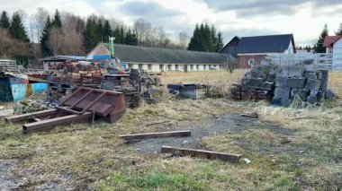 İhmal edilmiş hurda materyalleri ve gür yabani otlarla dolu uzun ve terk edilmiş bir sanayi bölgesini görüntülüyor.