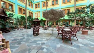 Bereketli yeşilliklerin, oturma düzenlerinin ve hareketli bir atmosferin olduğu sakin bir avlu..