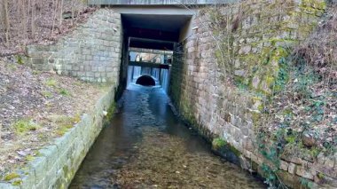Güzel, sakin bir su yolu manzarası. Büyüleyici bir taş kemerin altında, gür bir ormanlık alanda zarifçe akıyor.