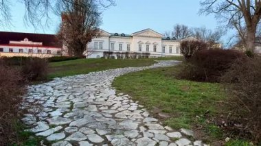 Manzaralı bir taş yol, yemyeşil alanların arasından geçip ziyaretçilere büyüleyici ve tarihi bir malikaneye doğru yol gösteriyor.