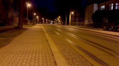 Gecenin köründe sakin, ıssız bir cadde. Yumuşak parlayan sokak lambaları ve farklı tramvay rayları sergileniyor.