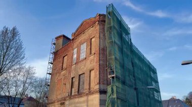 Tarihi bir tuğla bina yenileniyor, yeşil iskelelerle kaplı, inşaat işleri sergileniyor..