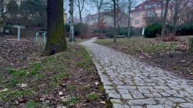 Huzurlu, dolambaçlı bir kaldırım taşı yolu, bereketli doğayla çevrili sakin bir park ortamında usulca dolanıyor.