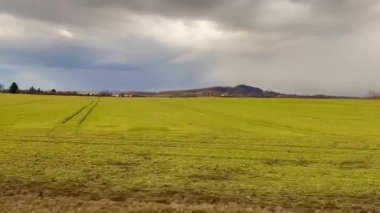 Canlı ve canlı yeşil bir alan, kasvetli bir gökyüzünün altındaki uzak, yuvarlanan tepelere doğru zarif bir şekilde uzanıyor.