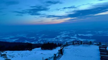 Gün batımında, bir dağın tepesindeki gözlem güvertesinden kar kaplı dağların ve parlak gökyüzünün akşam manzarası. Yüksek kalite 4k görüntü