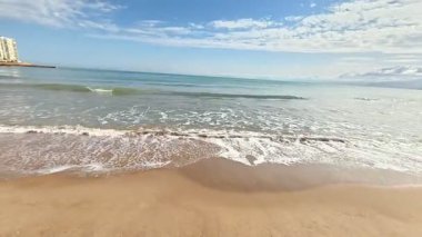 Yumuşak altın kumu, yumuşak dalgaları ve çarpıcı açık mavi gökyüzünü gösteren sakin bir sahil manzarası hayal edin.