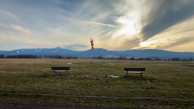 Huzurlu ve resimsel bir sahne sergilenen banklar, geniş açık alanlar, ve çarpıcı bir gökyüzünün altında görkemli dağlar