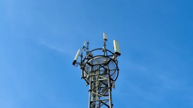 Antenli uzun bir iletişim kulesi mavi gökyüzüne doğru yükseliyor, modern teknoloji ve bağlantıyı simgeliyor.