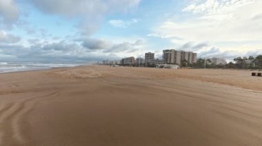 Huzurlu ve huzurlu bir sahil sahnesi yumuşak altın kumlar ve canlı dinamik bir gökyüzü altında kıyı mimarisi sergiliyor.