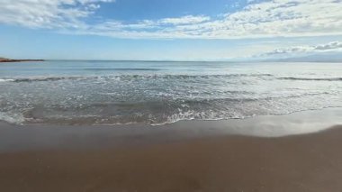 Huzurlu ve sakin bir sahil manzarası güzel sergiler sakin, nazik dalgalar parlak, berrak mavi bir gökyüzü altında parlıyor.