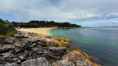 Huzurlu bir plajın nefes kesici manzarası, kayalık kıyılar ve canlı yemyeşil ile özenle çerçevelenmiş.