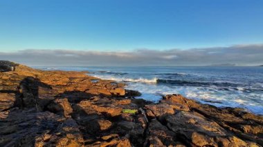 Engebeli, görkemli kayalar ve açık mavi bir gökyüzünün altında hafif dalgaların yer aldığı güzel, sakin bir deniz manzarası.