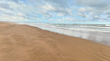 Yumuşak altın kumlardan oluşan sakin bir sahil manzarası, yumuşak dalgalar içeri akıyor, ve yukarıda canlı renkli bir gökyüzü.
