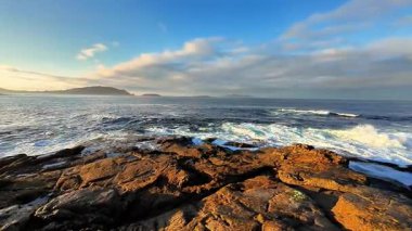 Nefes kesici bir manzara dalgaları sergiliyor dalgalar engebeli kayalara çarpıyor deniz kenarında canlı bir gündoğumu sırasında