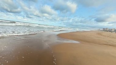 Sakin ve sakin bir sahil. Yumuşak dalgalar, büyüleyici bulutlu gökyüzünün altında yavaşça kıyıları sarıyor.