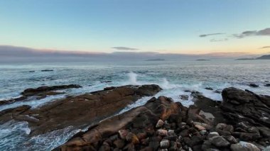 Alacakaranlıkta sakin bir okyanusun nefes kesici manzarası, dalgaların kayalık kıyı şeridine çarpması..