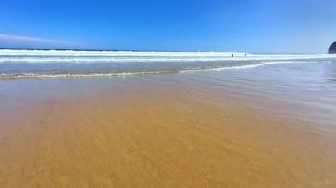 Huzurlu ve sakin bir sahil sahnesi. Parlak mavi gökyüzünün altında altın kıyıları ve nazik dalgaları davet ediyor.