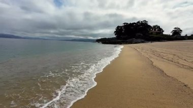 Huzurlu ve sakin bir sahil, son derece yumuşak kum, sakin sakin sular ve bulutlu bir gökyüzü.