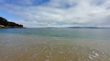 Güzel, sakin bir sahil sahnesi. Hafif dalgalar, geniş kumlu kıyılar ve yukarıda resim gibi bir gökyüzü.