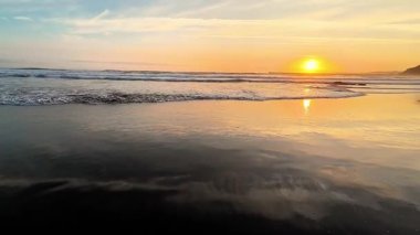 Nefes kesici altın bir günbatımı manzarası sahildeki sakin okyanus dalgalarını güzel bir şekilde yansıtıyor.