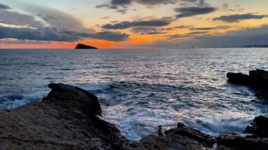 Nefes kesici bir günbatımı, dingin sularda ve yakınlardaki engebeli kayalarda canlı ve canlı renkler bırakır.