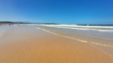 Güzel ve sakin bir sahil, yumuşak kumlu kıyılar, yumuşak okyanus dalgaları ve berrak mavi bir gökyüzü.