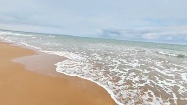 Sakin ve sakin bir sahil sahnesi, bulutlu bir günde kumlu sahilde usulca dalgalar sergiliyor.