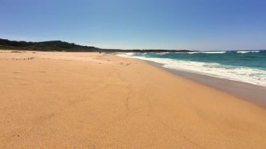 Huzurlu ve sakin bir plaj sahnesi yumuşak altın kum ve tam bir rahatlama için ideal hafif dalgalar sergiliyor.