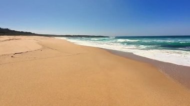 Parlak mavi gökyüzünün altında yumuşak dalgaları olan sakin kumlu bir sahil. Rahatlamak ve doğanın tadını çıkarmak için mükemmel.