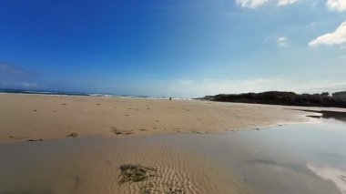 Yumuşak beyaz kum, çarpıcı yansımalar ve yukarıda canlı mavi bir gökyüzünün yer aldığı güzel, sakin bir sahil sahnesi.
