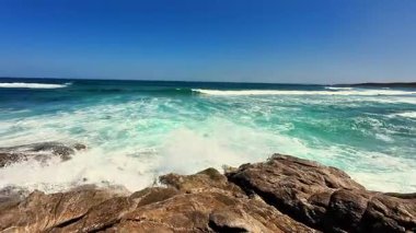 Güzel, güneşli bir günde engebeli kıyılara çarpan muhteşem okyanus dalgalarını hissedin.