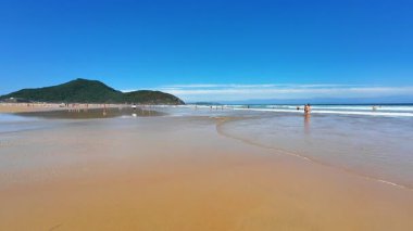 Büyüleyici bir sahil sahnesinde altın kum, kristal berrak su ve yukarıda güzel, canlı bir gökyüzü sergilenir.