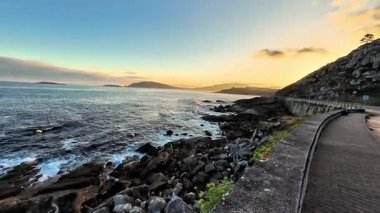 Gün batımında nefes kesen güzel bir sahil yolu, dalgalı okyanus dalgaları ve etrafındaki engebeli uçurumları gösteriyor.